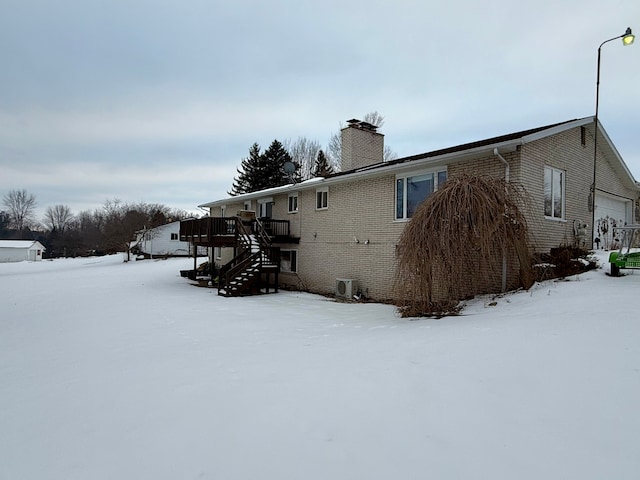 snow covered rear of property featuring a wooden deck and a garage