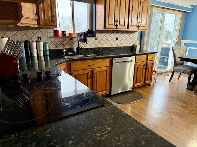 kitchen featuring sink, dark stone countertops, decorative backsplash, stainless steel dishwasher, and light wood-type flooring