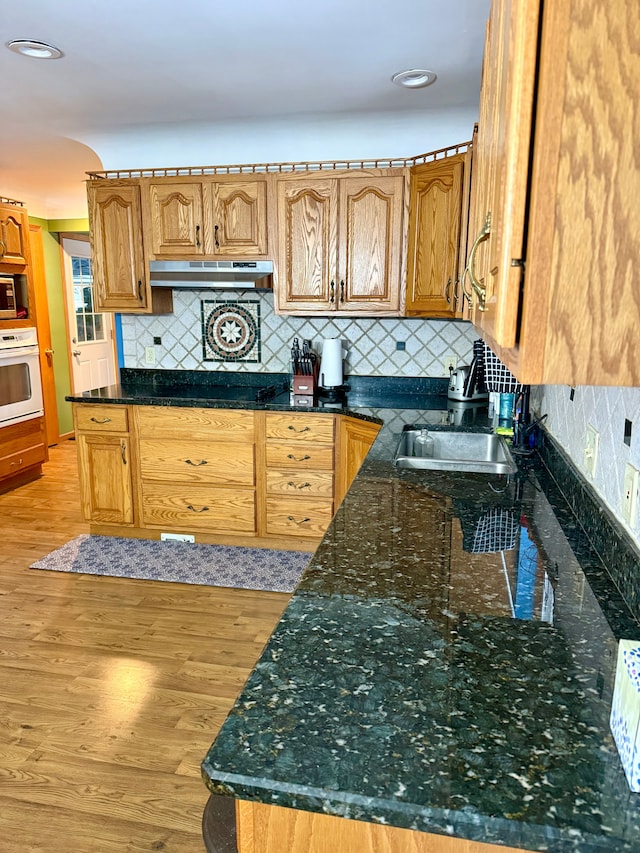 kitchen featuring white oven, sink, light wood-type flooring, and dark stone counters