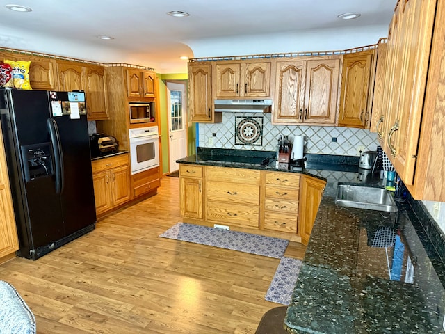 kitchen with sink, tasteful backsplash, black appliances, dark stone counters, and light wood-type flooring