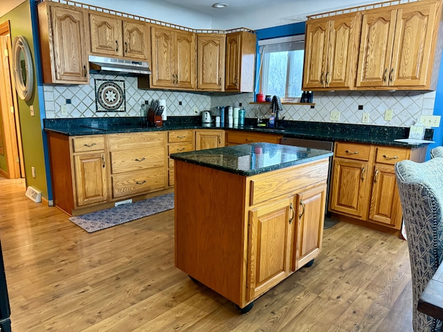 kitchen with sink, light hardwood / wood-style flooring, dark stone countertops, backsplash, and a kitchen island