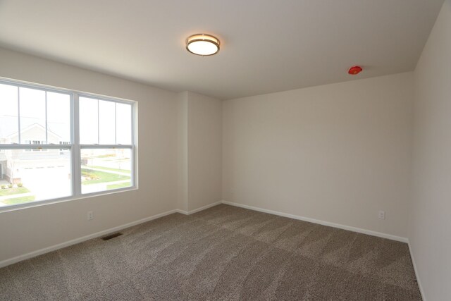 empty room with a healthy amount of sunlight, baseboards, carpet, and visible vents
