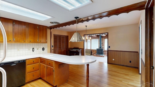 kitchen with black dishwasher, light hardwood / wood-style floors, decorative light fixtures, kitchen peninsula, and a wood stove