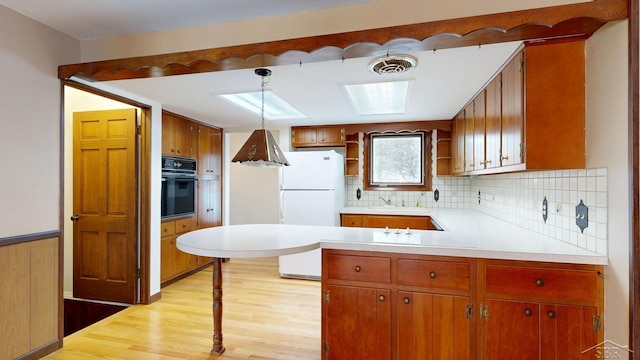 kitchen with hanging light fixtures, white fridge, decorative backsplash, oven, and light wood-type flooring