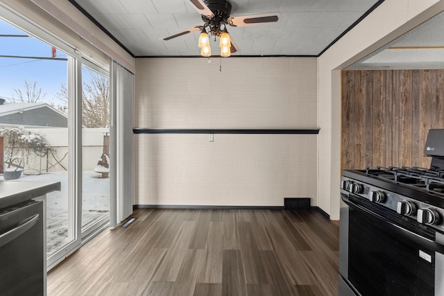 kitchen with brick wall, range with gas stovetop, wood-type flooring, stainless steel dishwasher, and ceiling fan