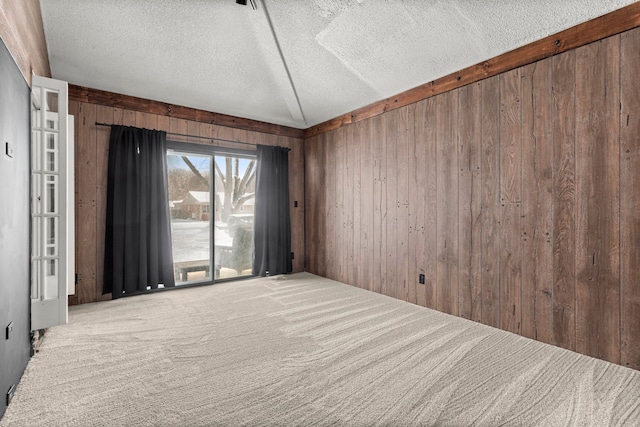 carpeted empty room featuring wooden walls, a textured ceiling, and vaulted ceiling