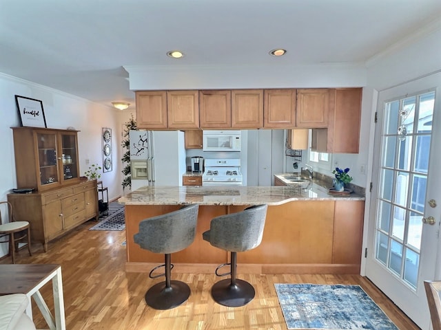 kitchen with light wood-type flooring, kitchen peninsula, light stone countertops, sink, and white appliances