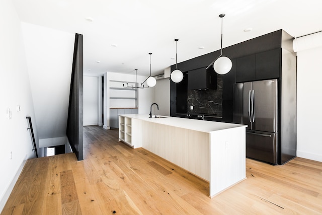 kitchen featuring sink, stainless steel fridge, hanging light fixtures, light hardwood / wood-style floors, and a center island with sink