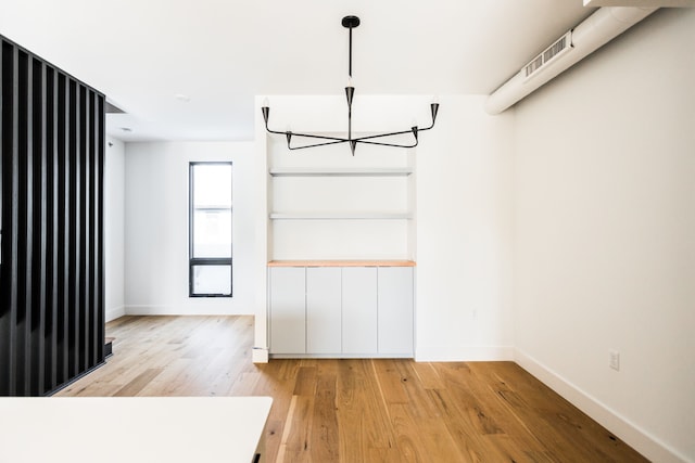 unfurnished dining area featuring an inviting chandelier and light hardwood / wood-style floors