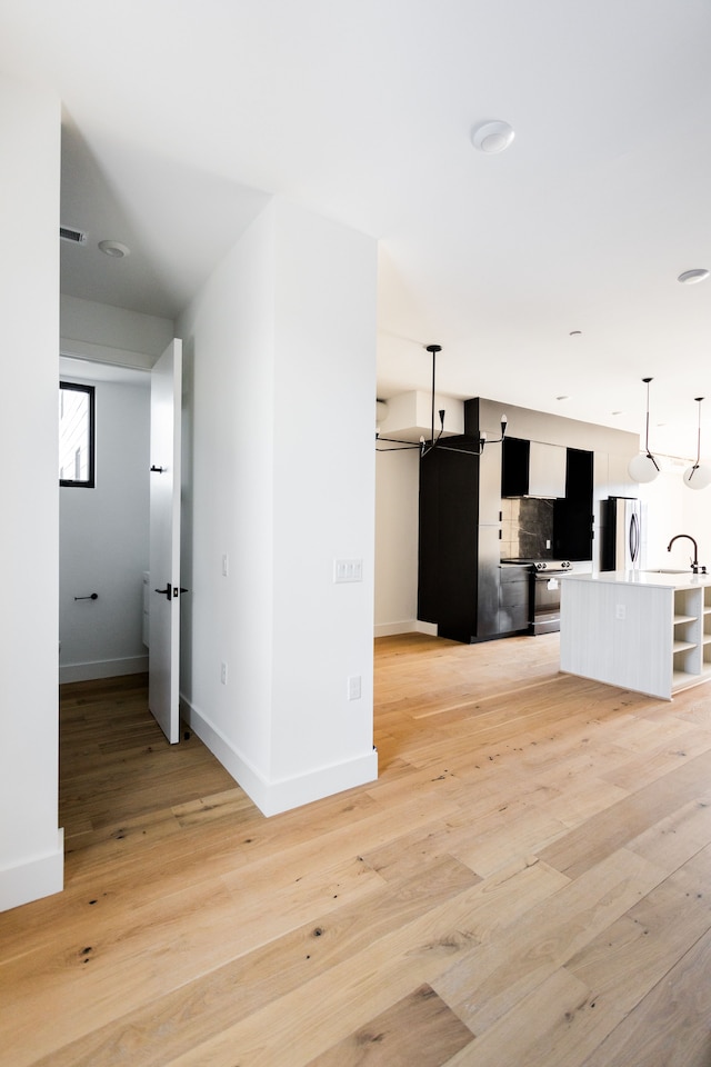 kitchen with sink, hanging light fixtures, fridge, an island with sink, and light wood-type flooring