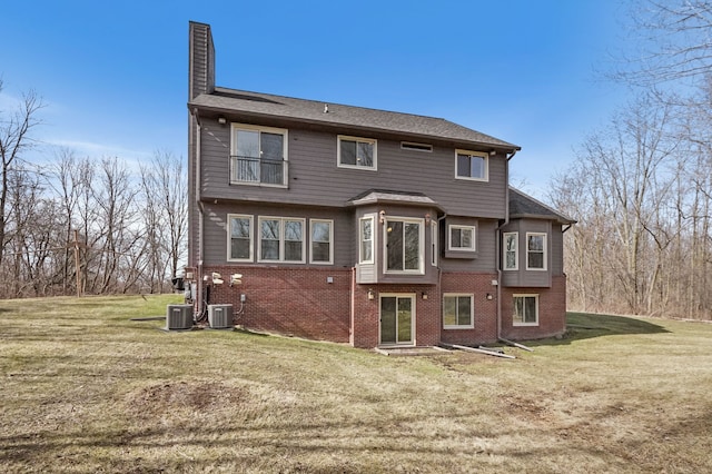 back of house featuring a yard, central AC unit, brick siding, and a chimney