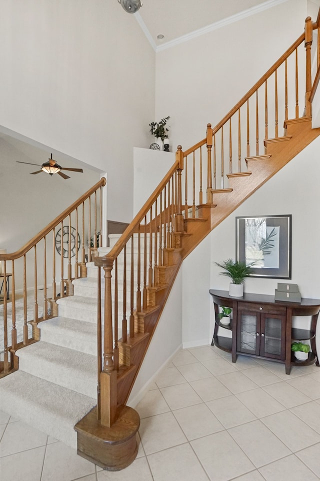 stairway featuring a ceiling fan, baseboards, tile patterned flooring, a towering ceiling, and crown molding