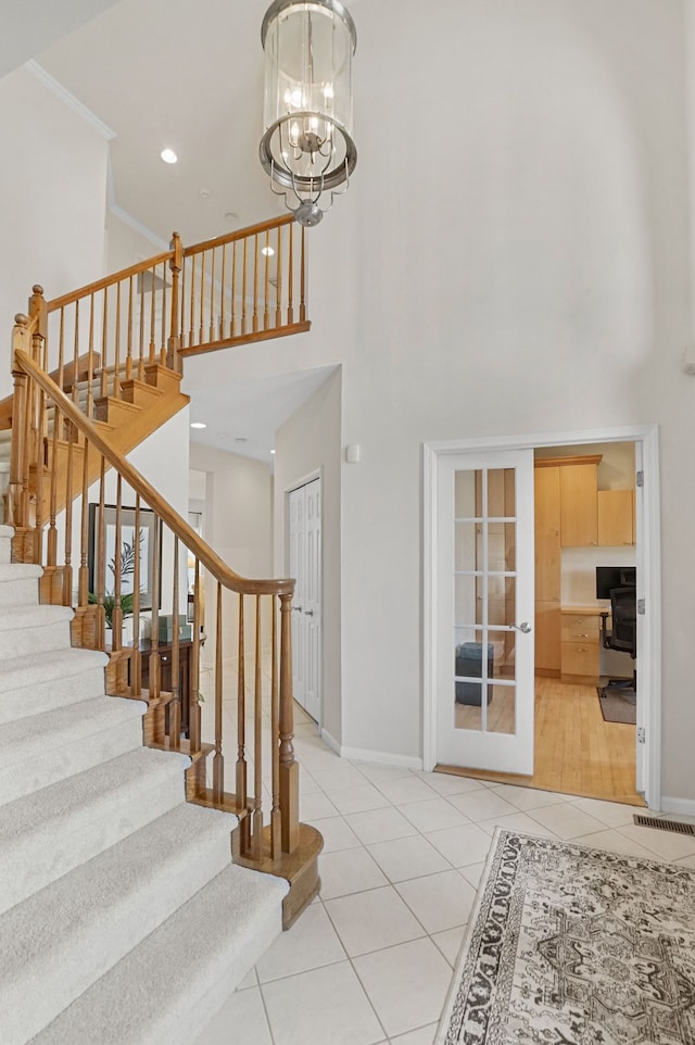 stairs with tile patterned flooring, crown molding, baseboards, an inviting chandelier, and a towering ceiling