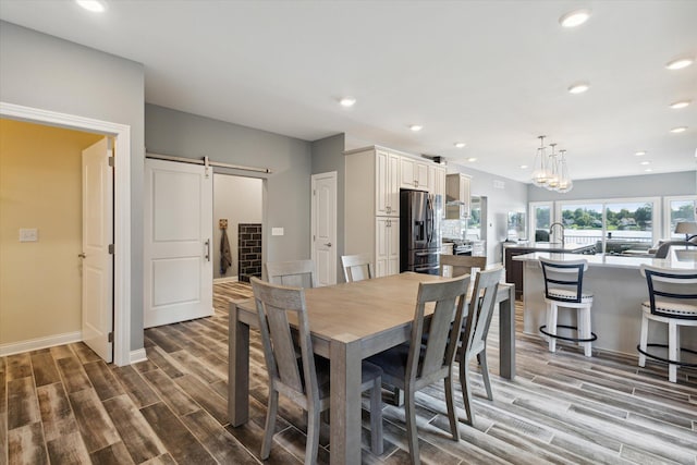 dining space with hardwood / wood-style flooring, a barn door, sink, and a notable chandelier