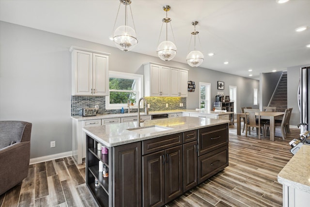 kitchen with sink, white cabinetry, dark brown cabinets, an island with sink, and decorative light fixtures