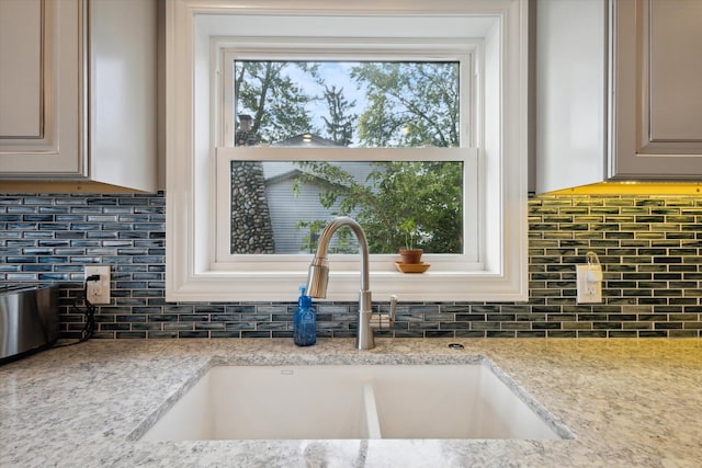 kitchen with light stone counters, sink, tasteful backsplash, and a wealth of natural light