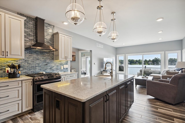 kitchen with double oven range, cream cabinets, pendant lighting, and wall chimney range hood