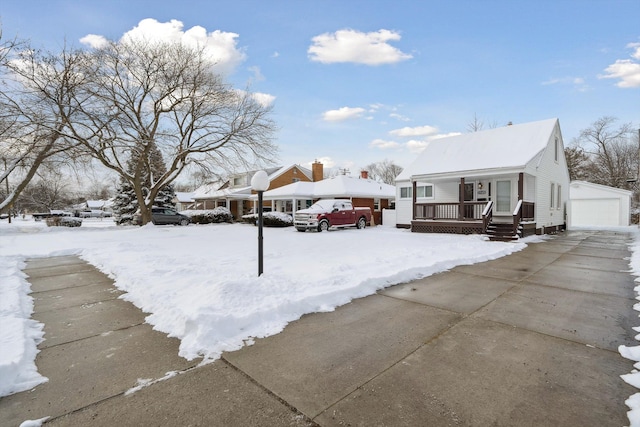 snowy yard featuring a garage, an outdoor structure, and a porch