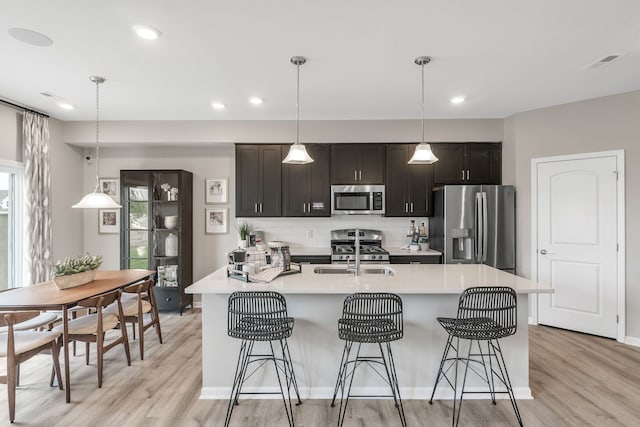 kitchen with a breakfast bar area, light wood-type flooring, light countertops, appliances with stainless steel finishes, and a kitchen island with sink