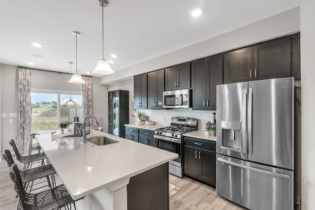 kitchen with a center island with sink, a sink, appliances with stainless steel finishes, light countertops, and decorative backsplash