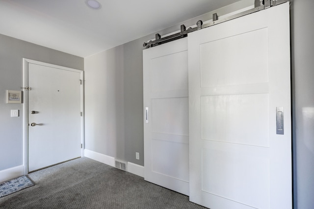 unfurnished bedroom with carpet flooring, visible vents, baseboards, and a barn door