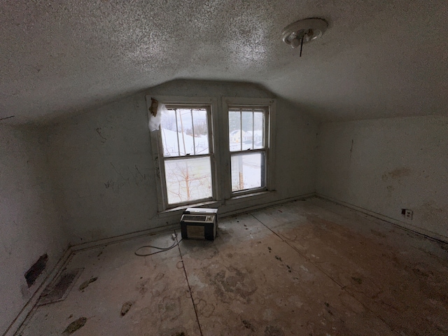 bonus room with vaulted ceiling, a wall unit AC, and a textured ceiling