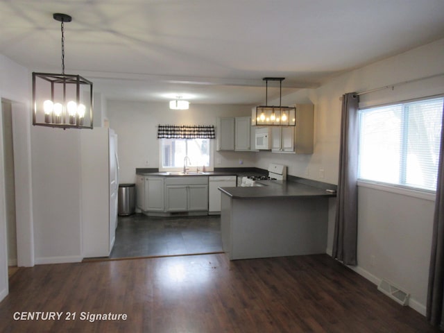 kitchen with sink, kitchen peninsula, white appliances, and decorative light fixtures