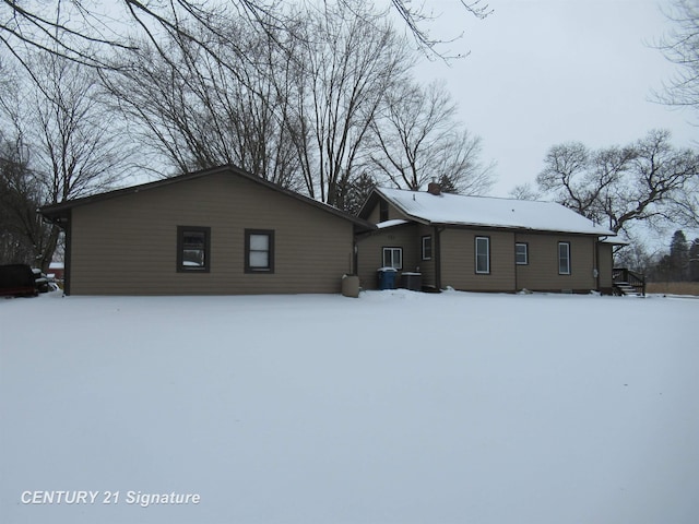 snow covered back of property featuring central AC unit