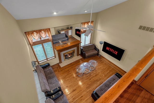 living room featuring vaulted ceiling, a tile fireplace, light hardwood / wood-style floors, and ceiling fan