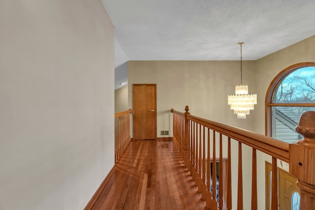 hall with an inviting chandelier, wood-type flooring, and a textured ceiling