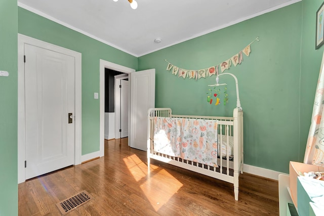 bedroom with baseboards, visible vents, wood finished floors, and ornamental molding