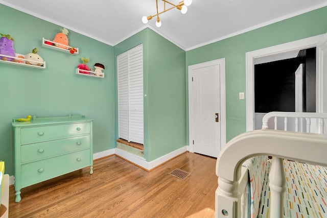 bedroom featuring baseboards, ornamental molding, visible vents, light wood-style floors, and a notable chandelier