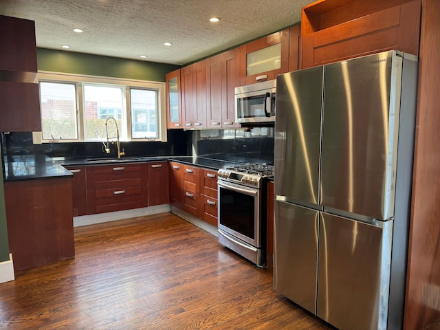 kitchen featuring a sink, dark countertops, appliances with stainless steel finishes, dark wood-type flooring, and glass insert cabinets