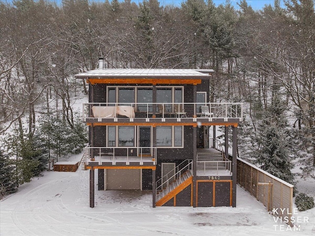 snow covered back of property with a garage and a balcony