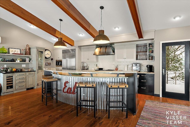 kitchen featuring decorative light fixtures, a breakfast bar area, built in refrigerator, a center island with sink, and wall chimney exhaust hood