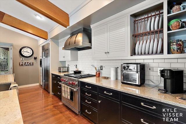 kitchen with wall chimney exhaust hood, light stone counters, tasteful backsplash, premium appliances, and hardwood / wood-style floors