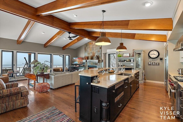 kitchen featuring sink, light stone counters, hanging light fixtures, dark hardwood / wood-style floors, and a kitchen island with sink