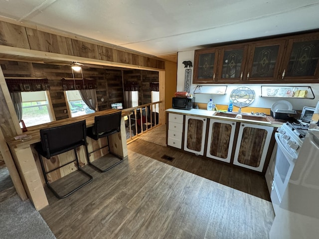 8210 N Johnson Rd, Irons, MI 49644 - kitchen featuring black microwave, dark brown cabinets, wooden walls, dark wood-style flooring, and glass insert cabinets