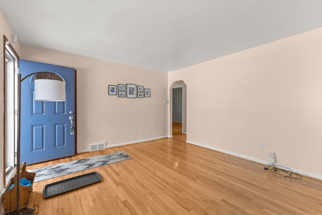 workout room with light wood-style floors, arched walkways, visible vents, and baseboards