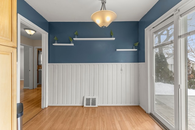 unfurnished dining area with wainscoting, visible vents, and wood finished floors