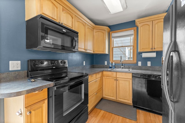 kitchen with light brown cabinets, a sink, black appliances, light wood finished floors, and dark countertops