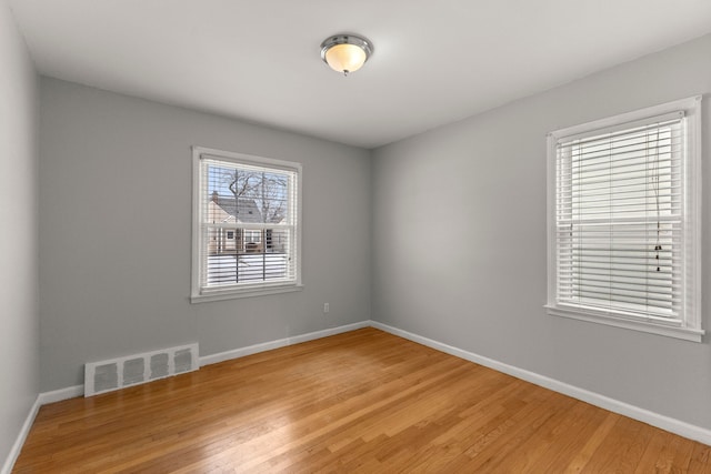 spare room with wood finished floors, visible vents, and baseboards