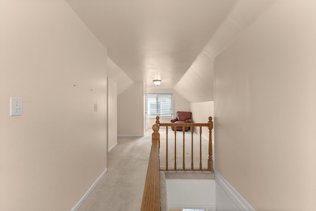 hall with baseboards, light colored carpet, vaulted ceiling, and an upstairs landing