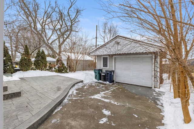 snow covered property featuring a detached garage, driveway, and an outdoor structure