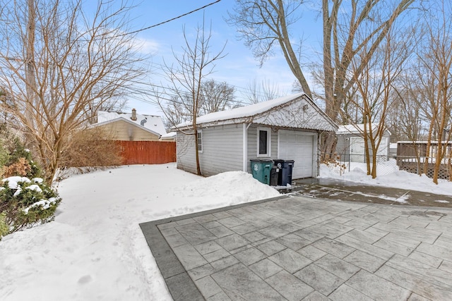 snow covered garage with a garage, driveway, and fence