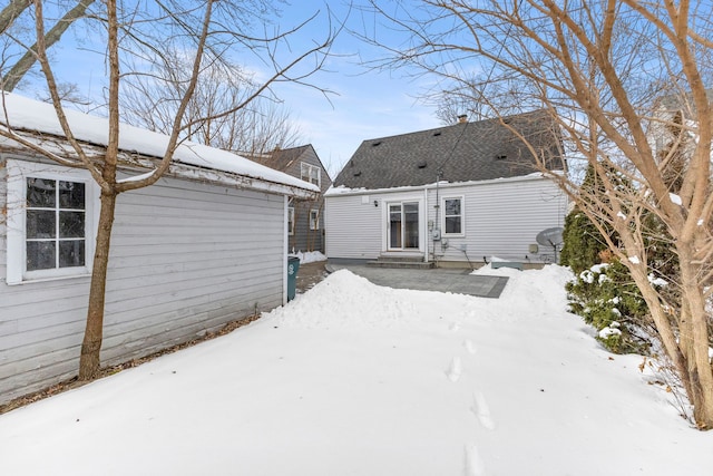 snow covered rear of property featuring entry steps and a shingled roof