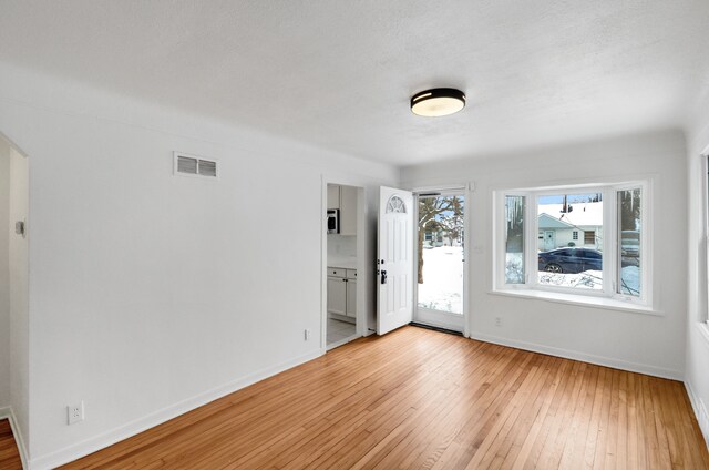 unfurnished room with a textured ceiling and light hardwood / wood-style floors