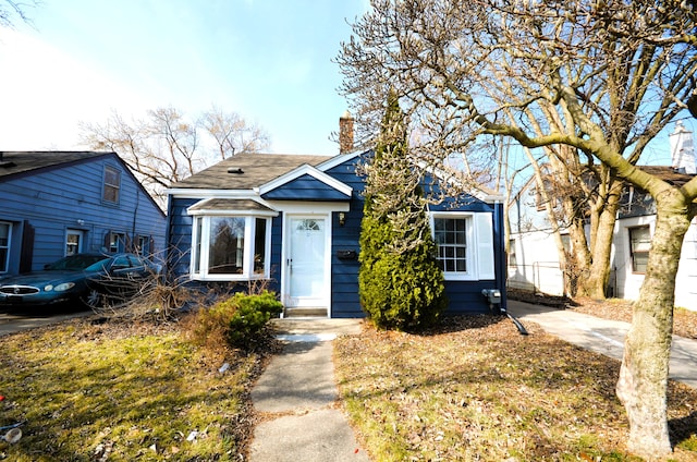 bungalow-style home with a chimney and a shingled roof