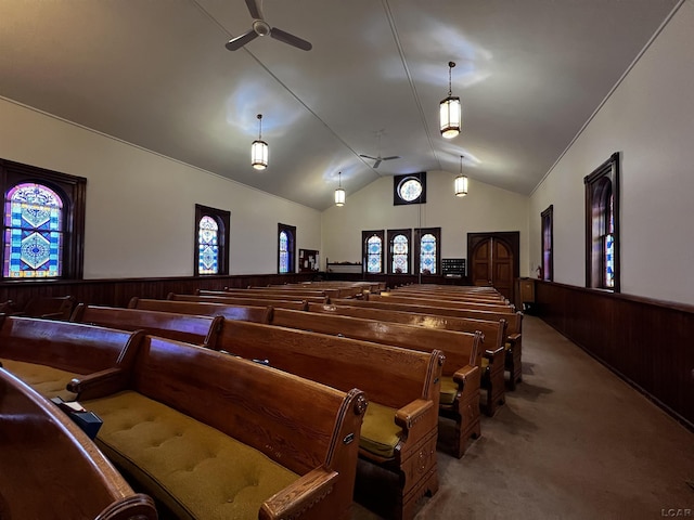 carpeted cinema room with ceiling fan, vaulted ceiling, and wood walls