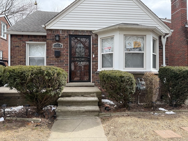 view of exterior entry featuring brick siding and roof with shingles